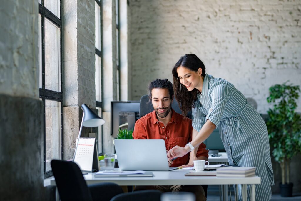 A female coworker assisting a male coworker with a task on the computer